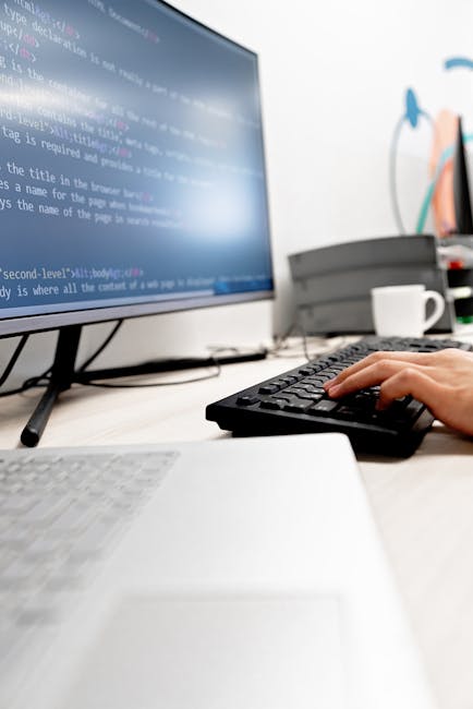 A photograph shows a close-up of a computer screen displaying lines of HTML code with various tags and links in a professional dark-themed coding environment. The code includes elements such as <h